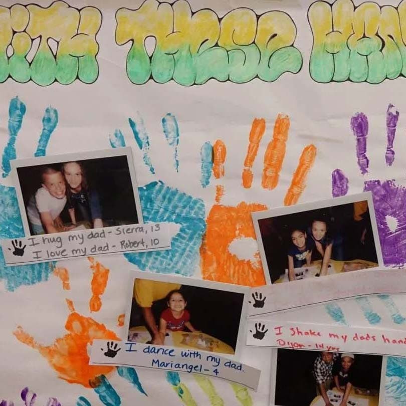 A colorful poster features handprints in green, blue, orange, and purple paint, along with four polaroid pictures of kids with their dads. Each picture has handwritten notes like "I hug my dad," "I love my dad," "I dance with my dad," and "I shake my dad's hand.