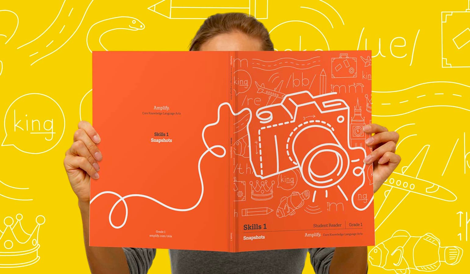 Person holding an open book with an illustrated camera on the cover against a yellow background with various white doodles. The book's title reads "Skills 1 Snapshots" and "Student Reader Grade 1" is listed at the bottom right.