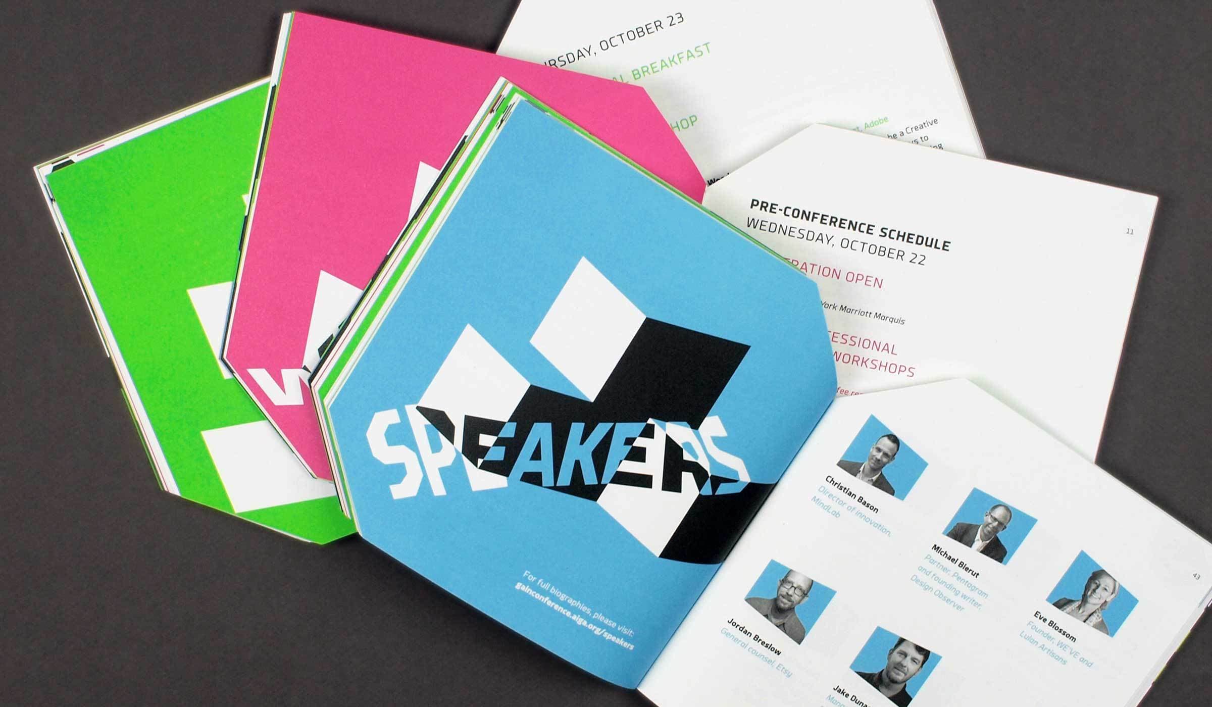 A stack of colorful conference booklets is displayed on a table. The booklets are in bright blue, green, and pink covers. The blue booklet has the word "SPEAKERS" printed on it, while the green booklet says "WA". The pages inside show schedules and speaker photos.