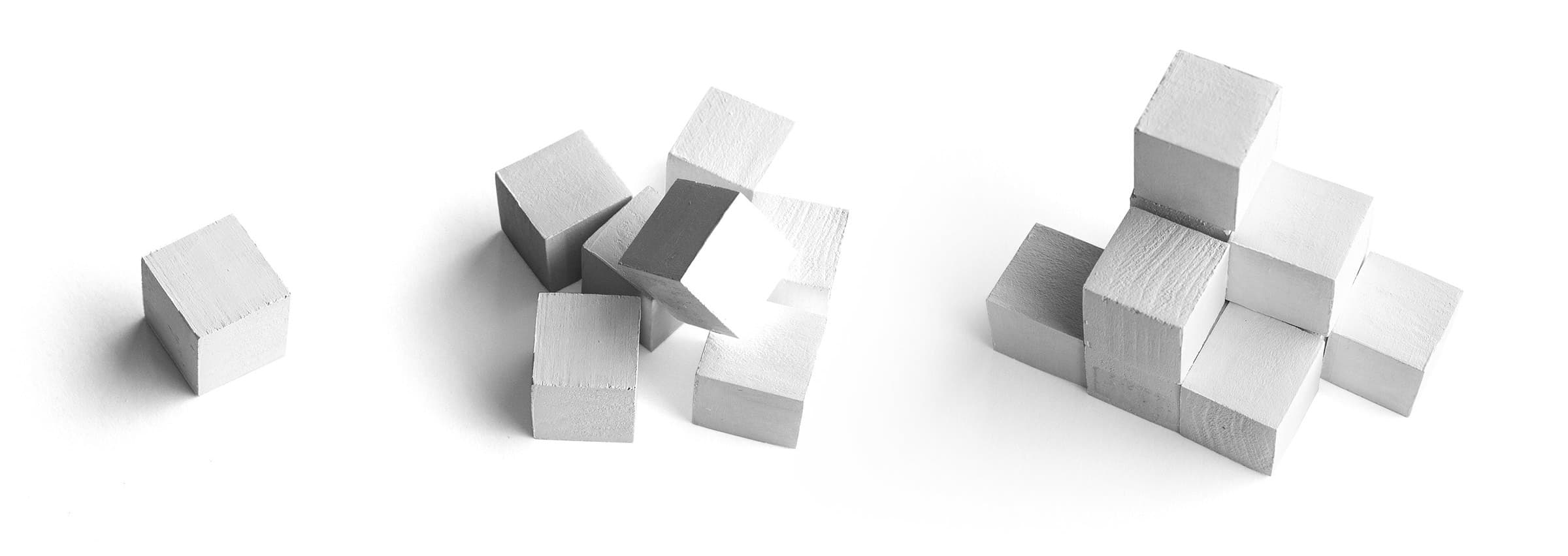 Three stages of wooden cube arrangement: on the left, a single cube; in the middle, several cubes randomly stacked; on the right, cubes neatly assembled into a structured, stepped formation. Background is plain white.