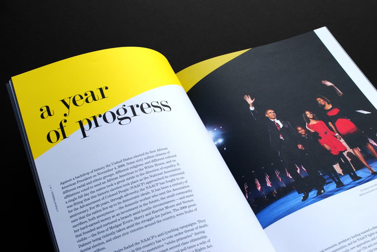 An open magazine showing a two-page spread. The left page has a large yellow section at the top with the text "a year of progress." The right page features a photo of four people standing on stage, waving, with U.S. flags in the background.