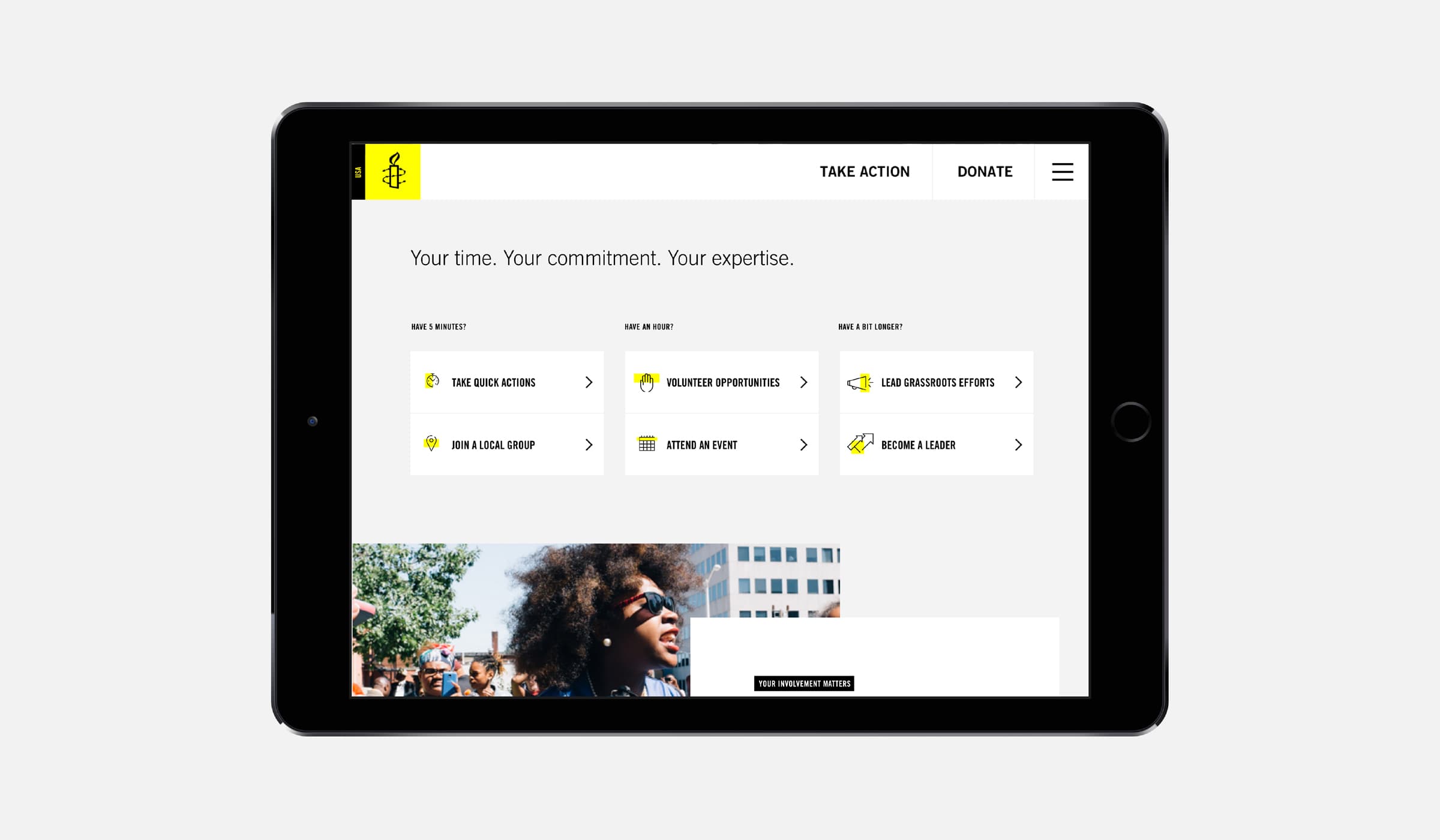 A tablet screen displaying a website with a navigation bar featuring "Take Action" and "Donate" options. The page has categories such as "Take Direct Action" and "Become a Leader." A photo at the bottom shows a person with sunglasses and an afro enjoying an outdoor event.