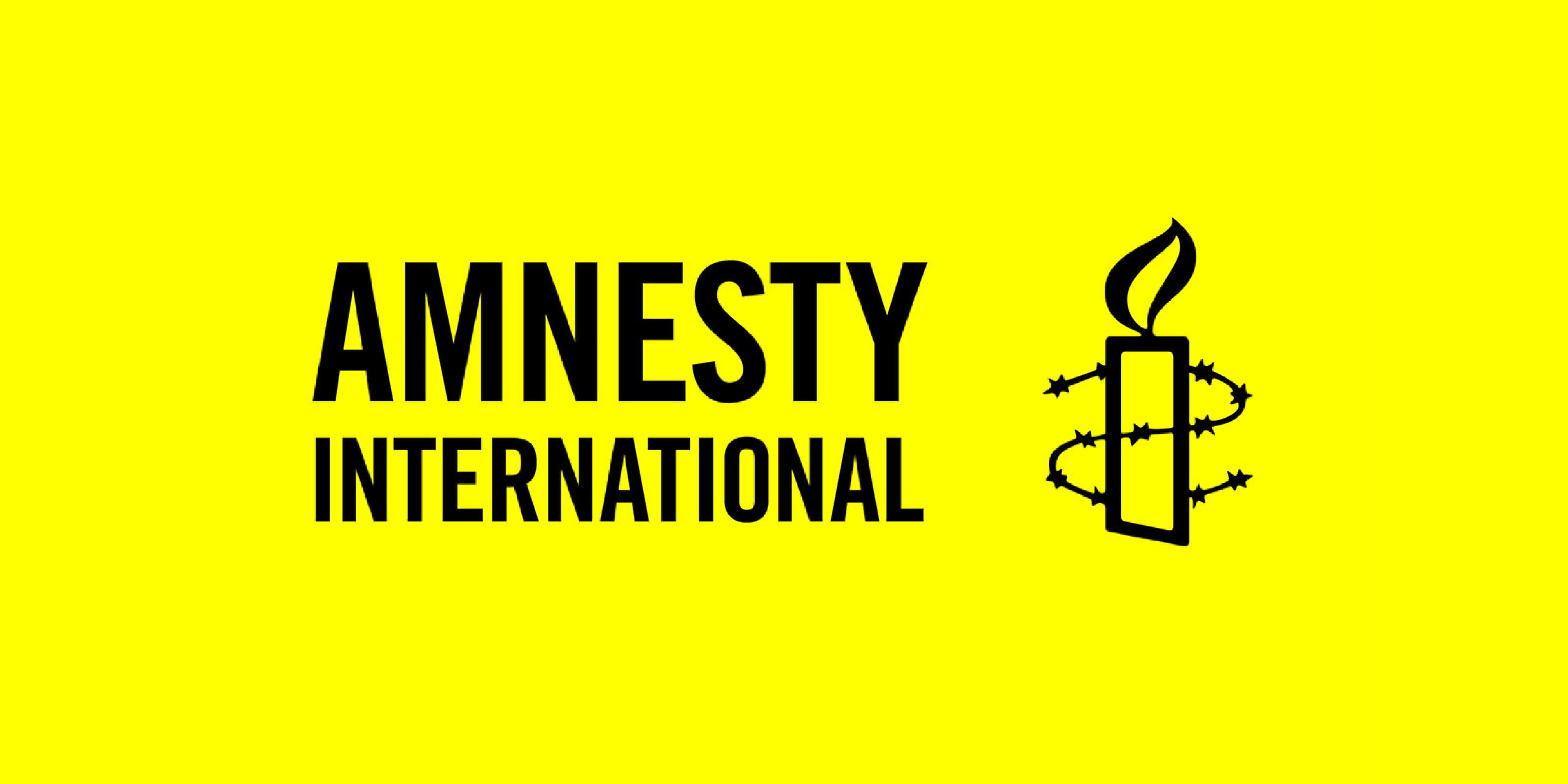 The image shows the logo of Amnesty International, featuring a bright yellow background with black text reading "AMNESTY INTERNATIONAL." To the right is an icon of a candle surrounded by barbed wire, representing the organization's commitment to human rights.