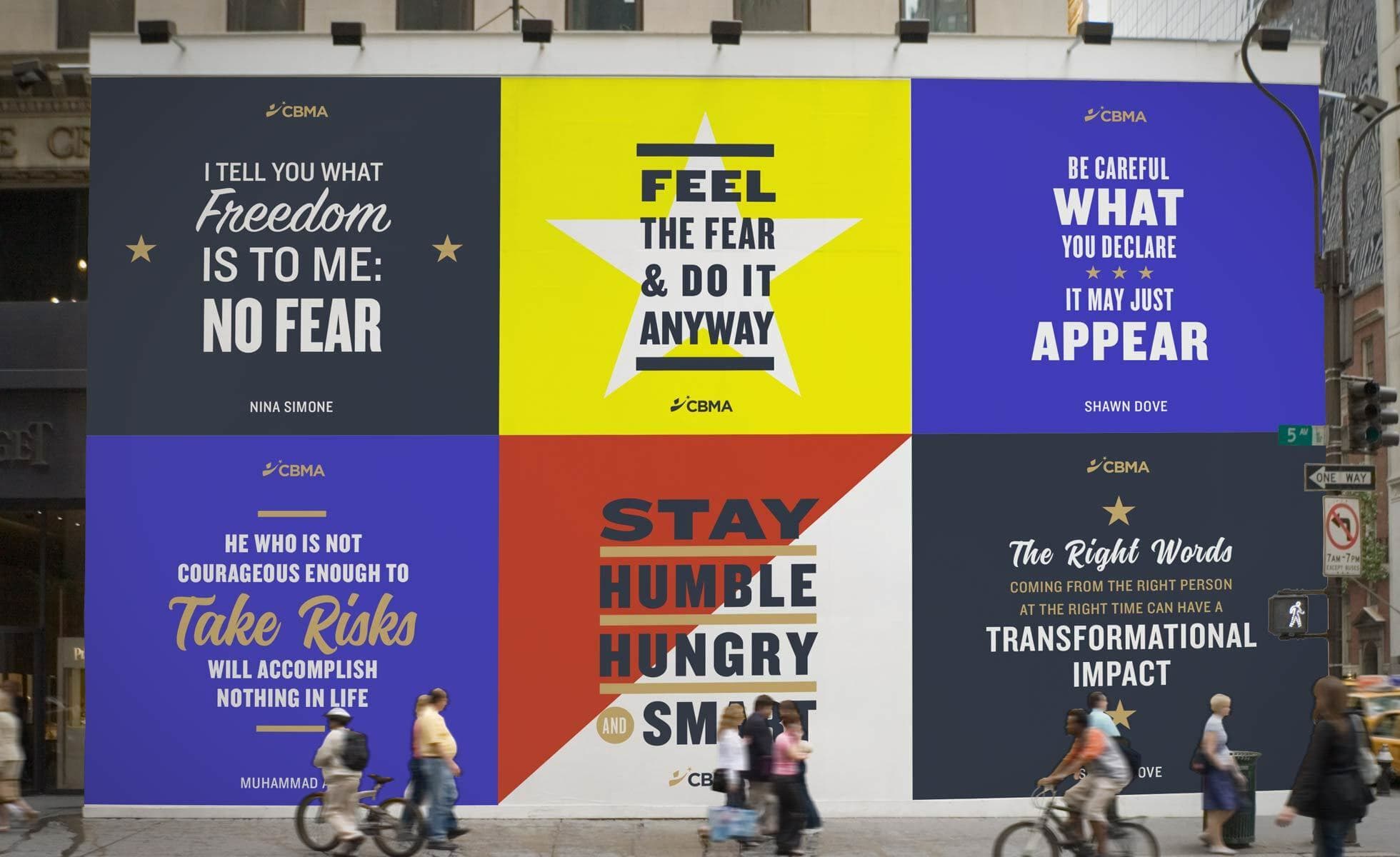 A wall displays six motivational posters with quotes. Each poster features bold, colorful designs and varied typography. Pedestrians pass by on the sidewalk, some on foot and some on bicycles, adding movement to the street scene.