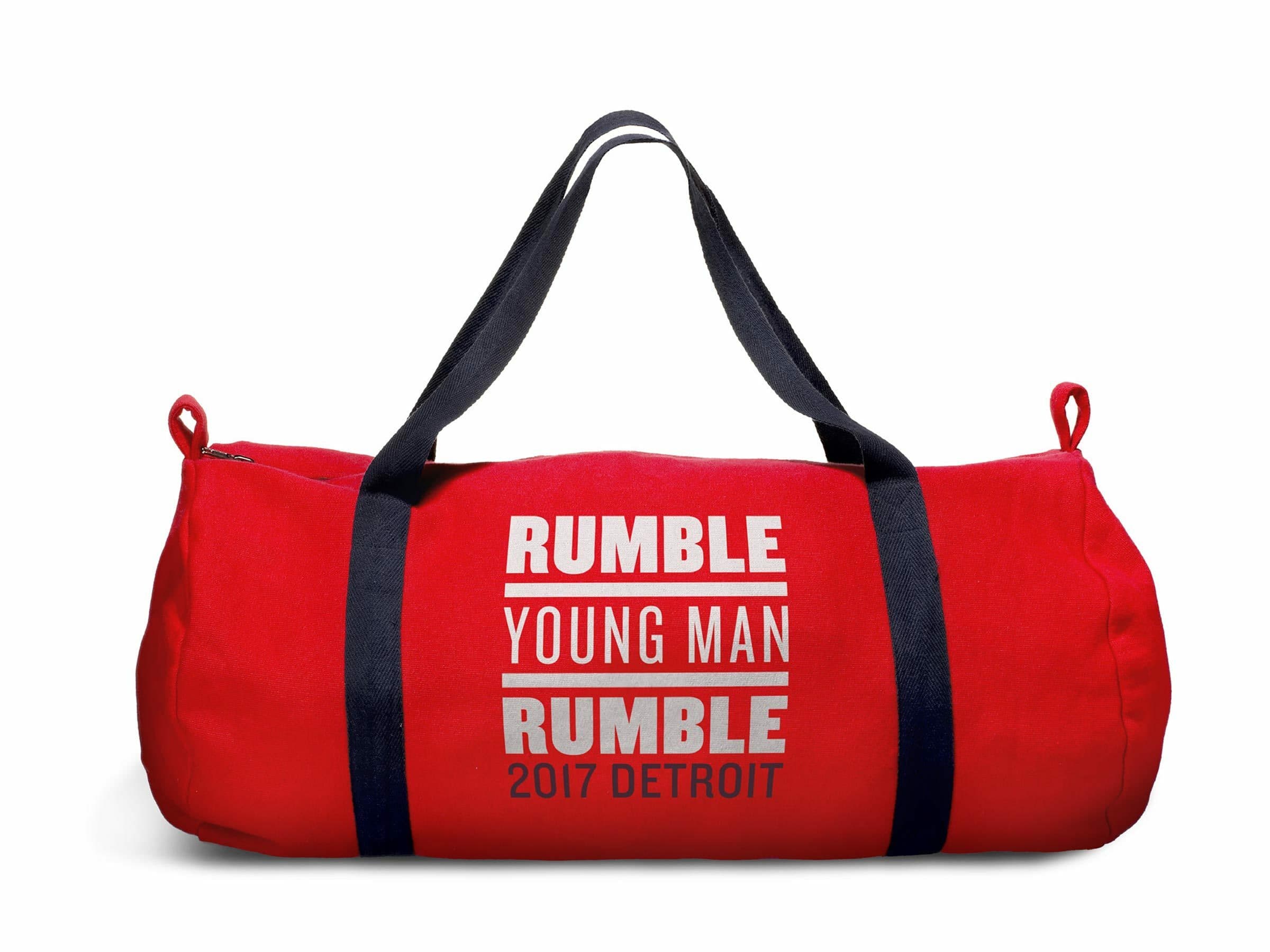 A red duffel bag with black straps displays white text that reads, "Rumble Young Man Rumble 2017 Detroit" on its side. The bag is cylindrical in shape with zipper closures on both ends.