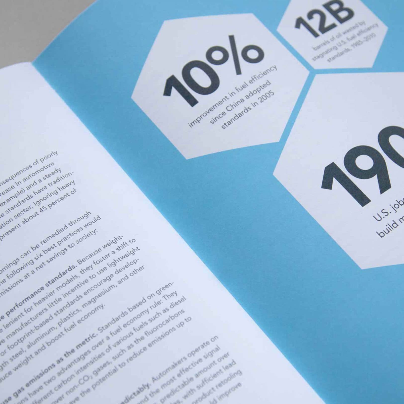 A close-up of an open booklet, displaying text and statistics on a blue background. Prominent text includes "10%" referencing fuel efficiency improvement, "12B", and "190K U.S. jobs". The page on the left has several paragraphs of smaller black text.