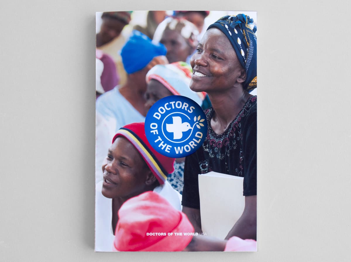 A booklet with the title “DOCTORS OF THE WORLD” features a cover image of smiling individuals, primarily women, some wearing headscarves. The focus is on a woman in a black dress, holding a folder. The background shows a group of people in colorful attire.
