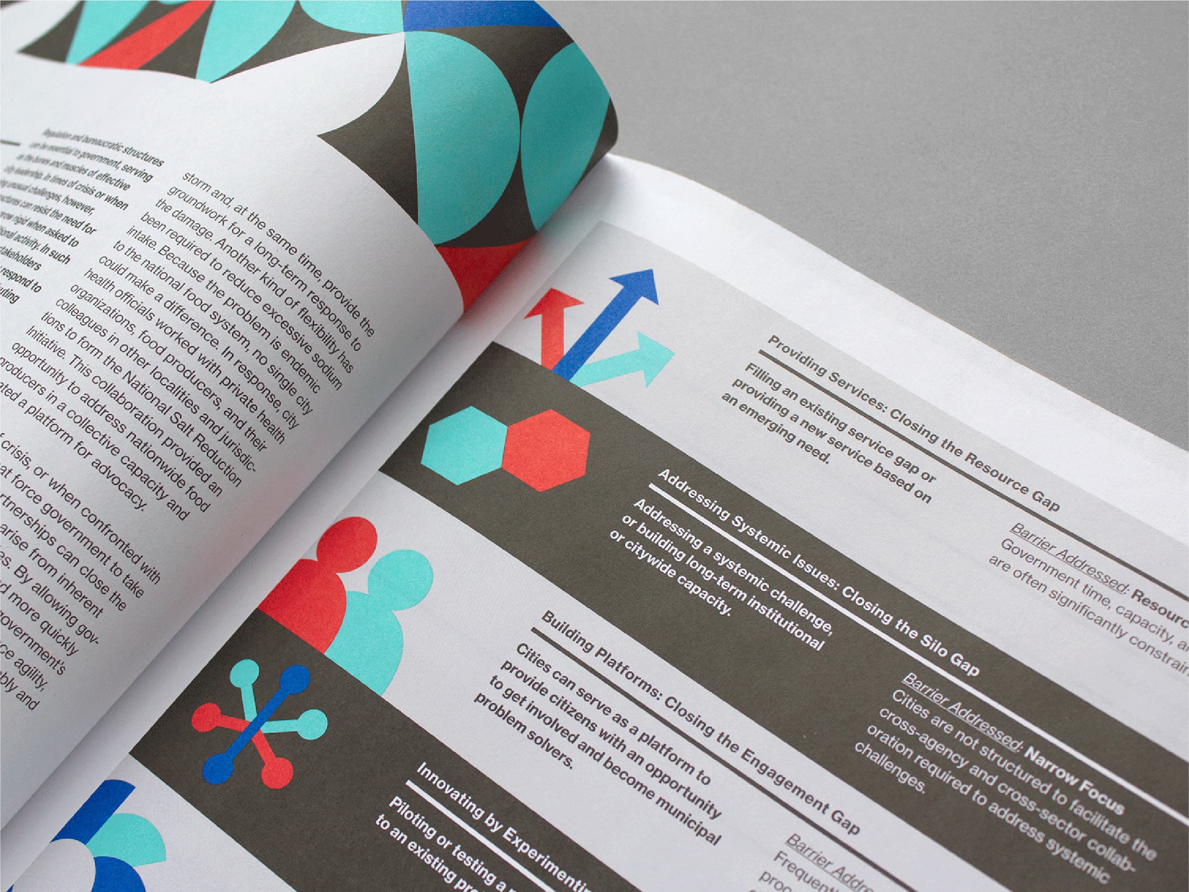 Close-up of a magazine or brochure opened to a page containing text and colorful graphics. The designs include abstract shapes such as circles, arrows, and hexagons in red, blue, and teal. The layout is organized with sections of text and visual elements for emphasis.