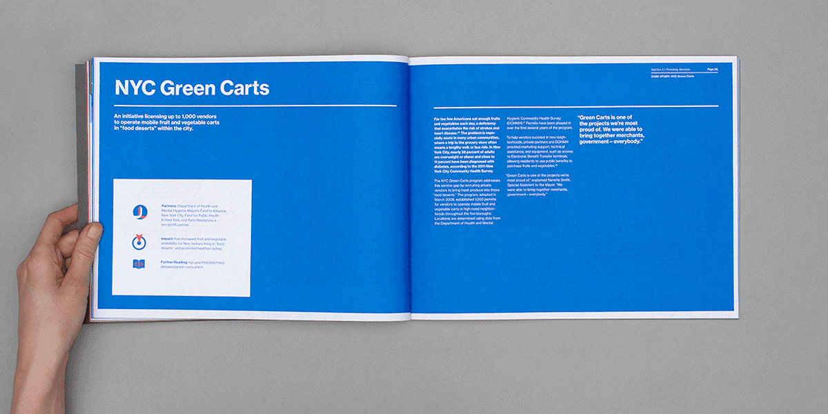 A person is holding an open book displaying a two-page spread titled "NYC Green Carts." The left page features text and small icons on a blue background. The right page includes more text and quotes on the same blue background.