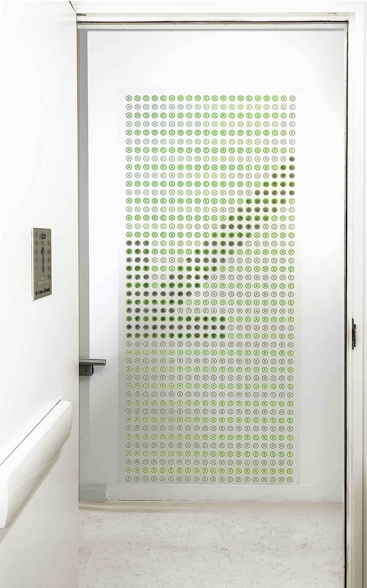 A white hallway with a glass door covered in a pattern of small green smiley faces arranged in a gradient from dense at the bottom left to sparse at the top right.