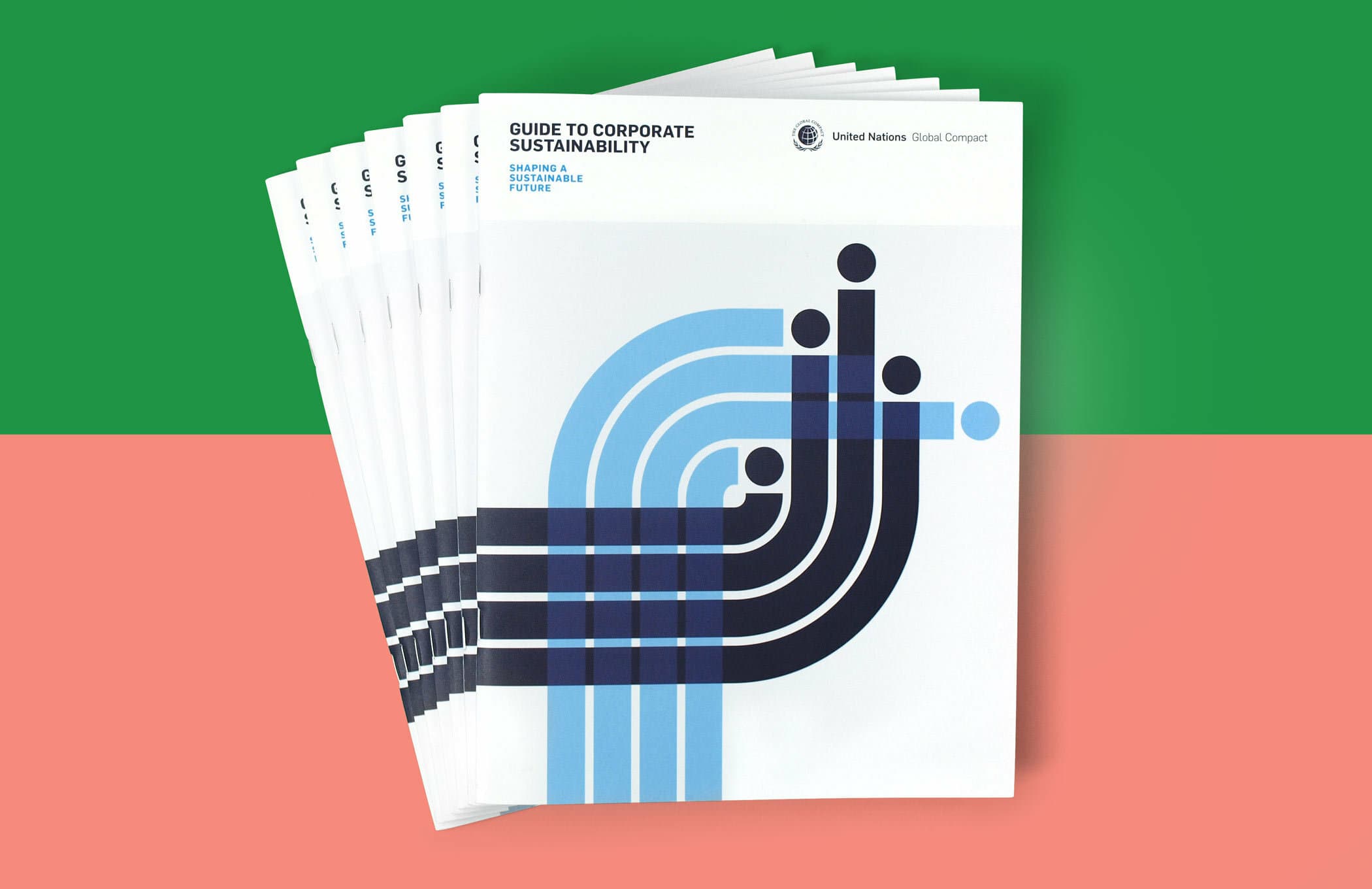 Stack of booklets titled "Guide to Corporate Sustainability" with a United Nations Global Compact logo. The cover features an abstract geometric design in blue and black on a white background. The background of the image is divided into green and pink sections.