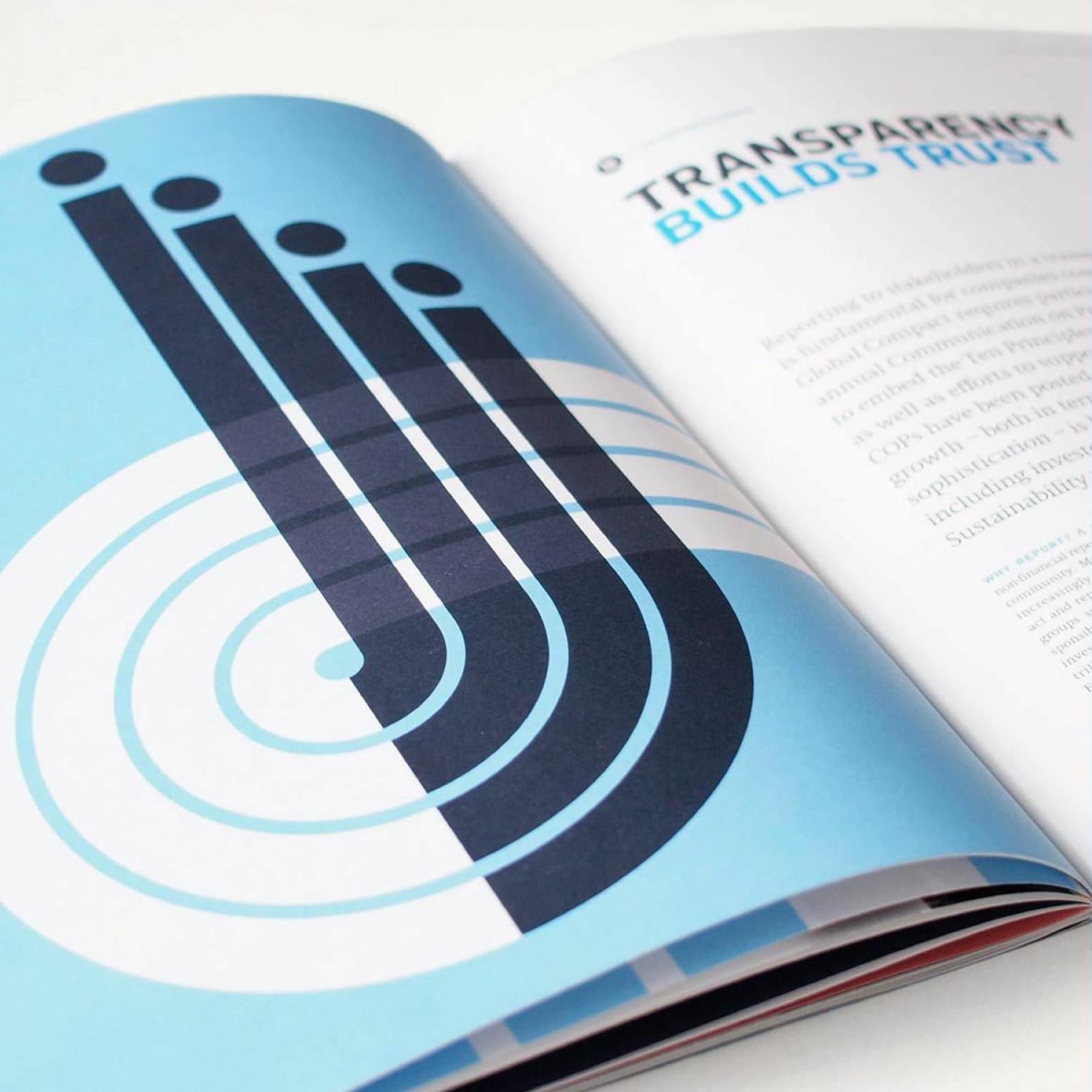 A magazine lies open, displaying a page with a geometric abstract design of intersecting lines and circles in dark blue and white on a light blue background. The opposite page features the title "TRANSPARENCY BUILDS TRUST" along with text paragraphs.