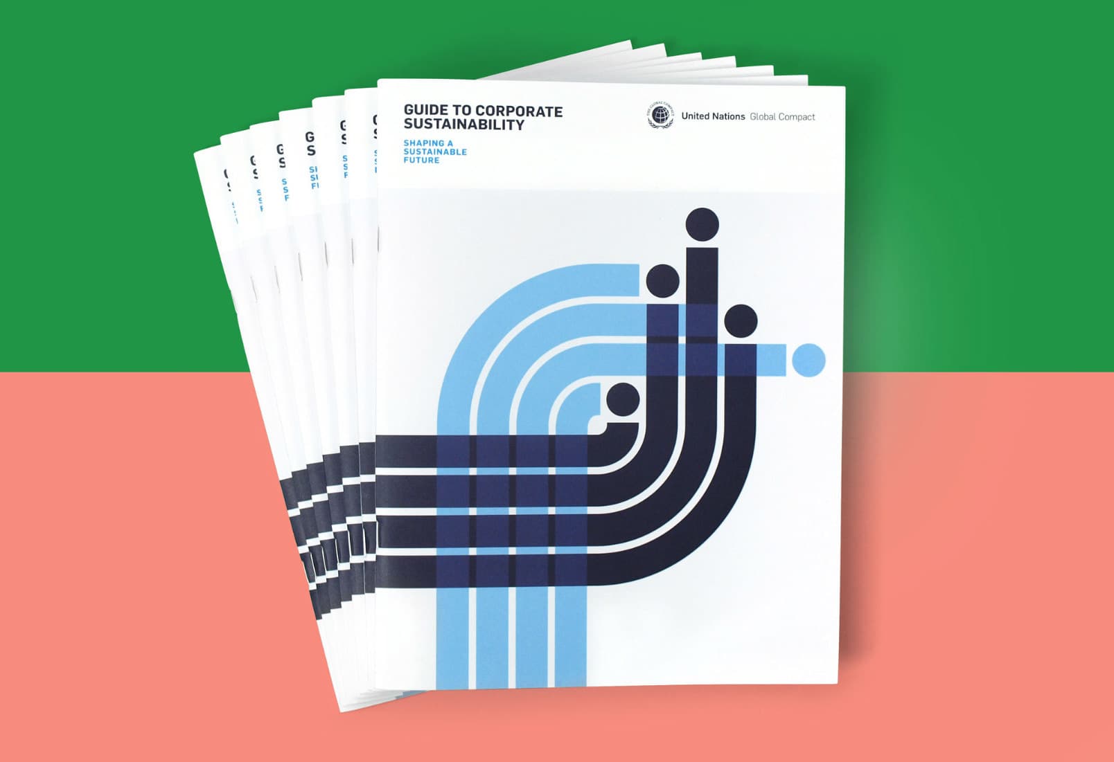 A stack of brochures titled "Guide to Corporate Sustainability" with abstract blue, black, and gray design elements on the cover. The background is divided into green and pink sections. The brochures feature the United Nations Global Compact logo.