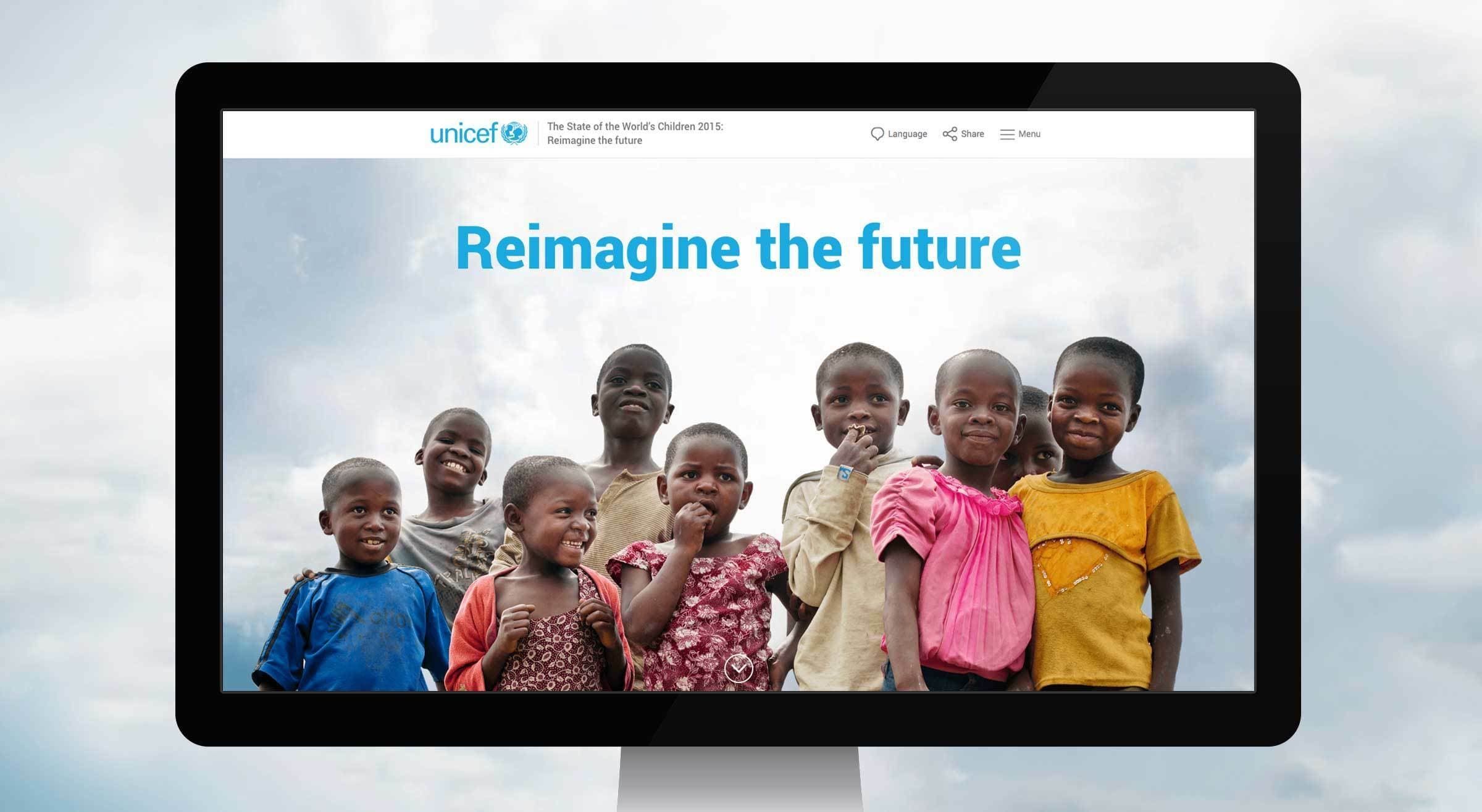 A computer monitor displays a UNICEF website page with the title "Reimagine the future." The screen shows a group of smiling children of diverse ages standing closely together outdoors under a cloudy sky.