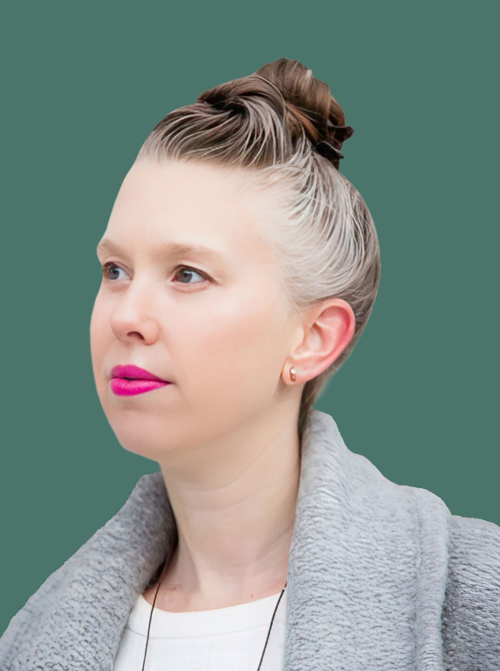 A person with pale skin and bright pink lipstick, hair in a bun with gray streaks, wearing a light gray textured coat and white top, stands against a solid teal background, looking slightly to the left.