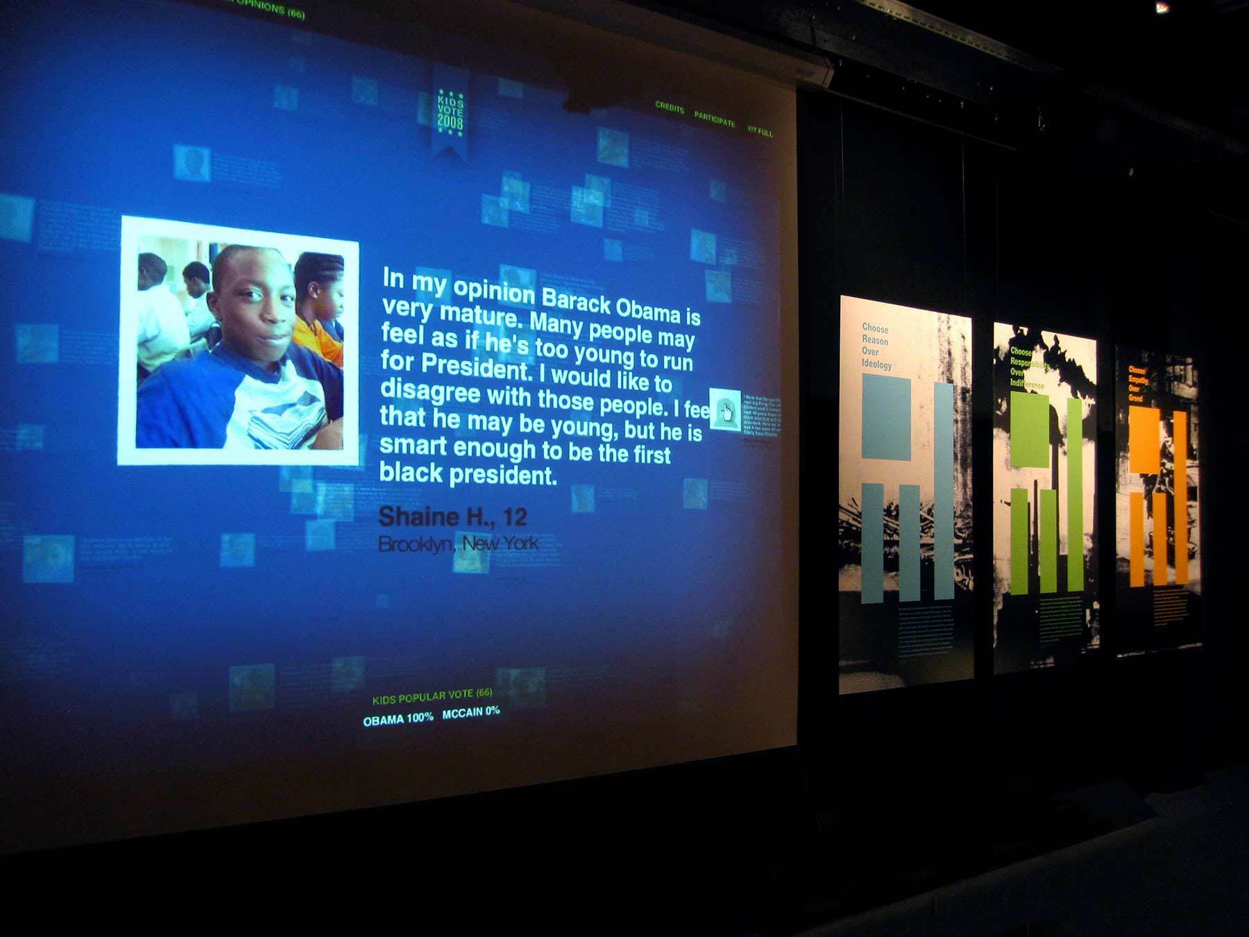 A display wall with a projection screen featuring a message from Shaine H., age 12, expressing support for Barack Obama as President. Beside the screen, there are various posters with images and graphs. The setting appears to be an educational exhibit.
