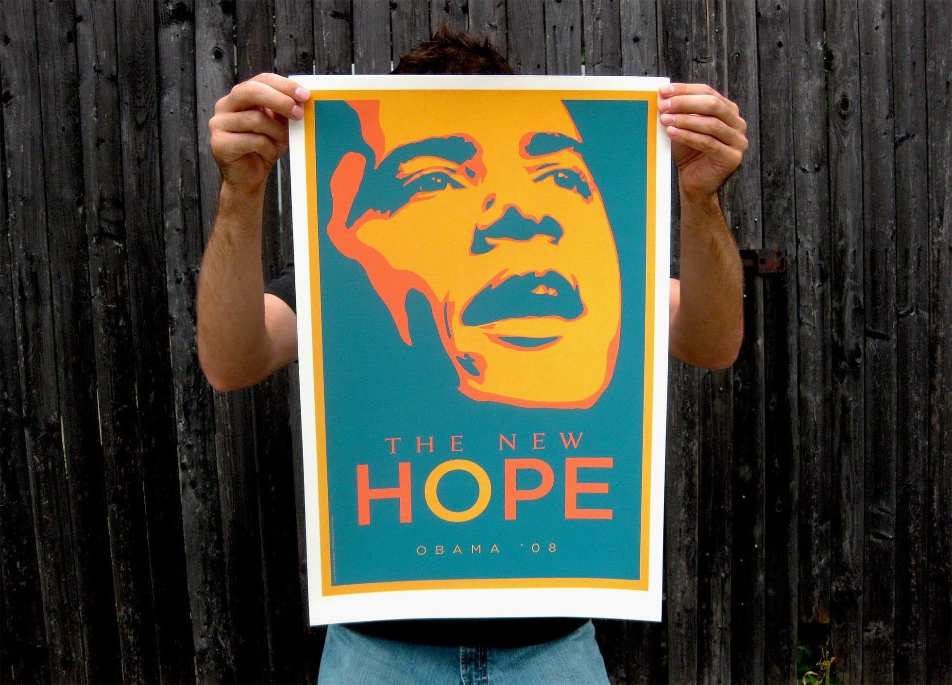 A person holds up a poster featuring a stylized image of Barack Obama in shades of orange and yellow against a teal background. The poster includes the words "THE NEW HOPE" and "Obama '08" at the bottom. The background consists of dark wooden planks.