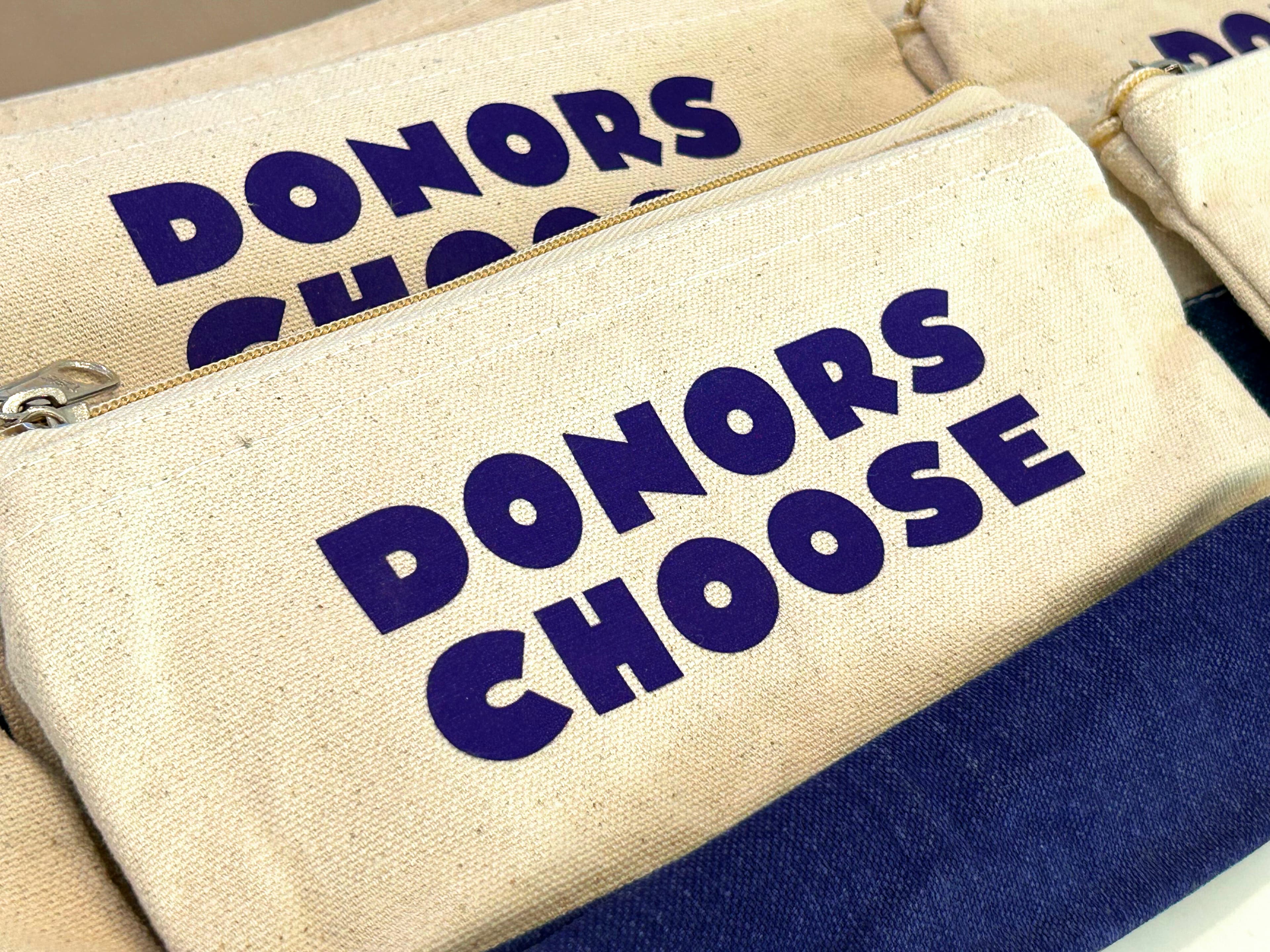Several beige zippered pouches with the words "DONORS CHOOSE" printed in bold, purple letters are neatly arranged side by side.