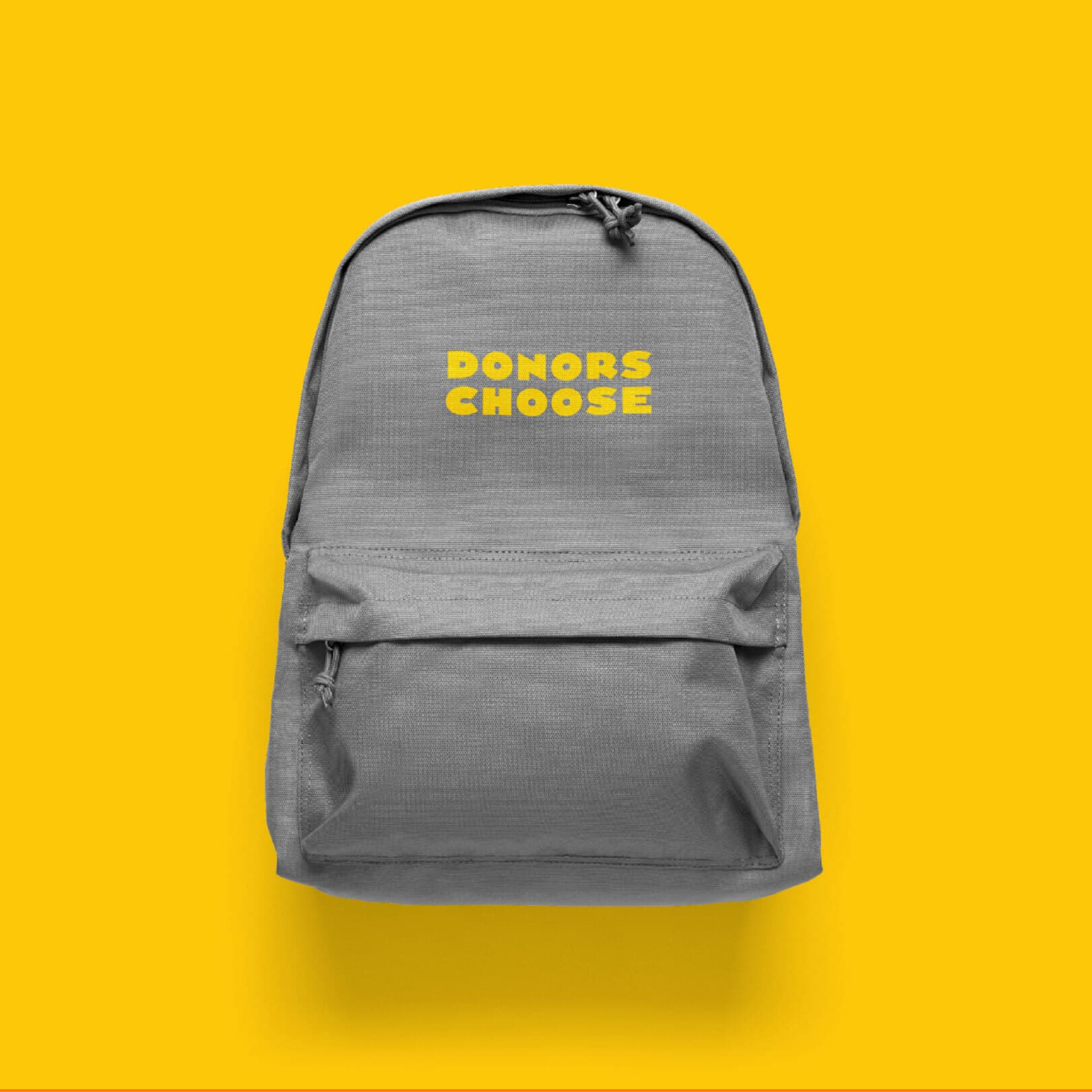 A gray backpack with the words "DONORS CHOOSE" printed in yellow on the front pocket sits against a bright yellow background. The backpack has a front zipper pocket and a drawstring at the top.