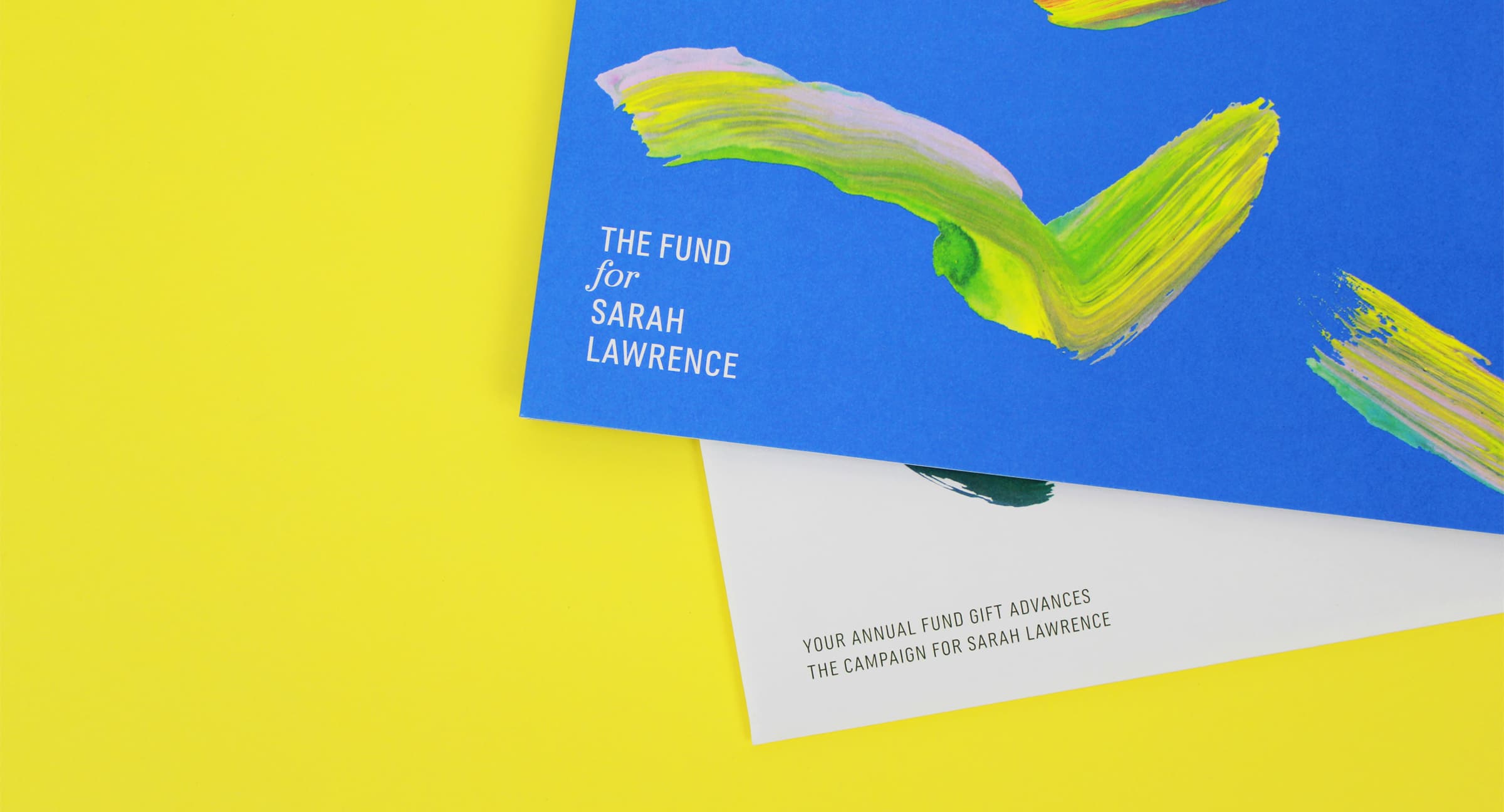 Two colorful flyers are stacked on a yellow surface. The top flyer is blue with bold green and yellow brushstrokes, and the text "The Fund for Sarah Lawrence." The bottom flyer is white with smaller text reading "Your Annual Fund Gift Advances The Campaign for Sarah Lawrence.