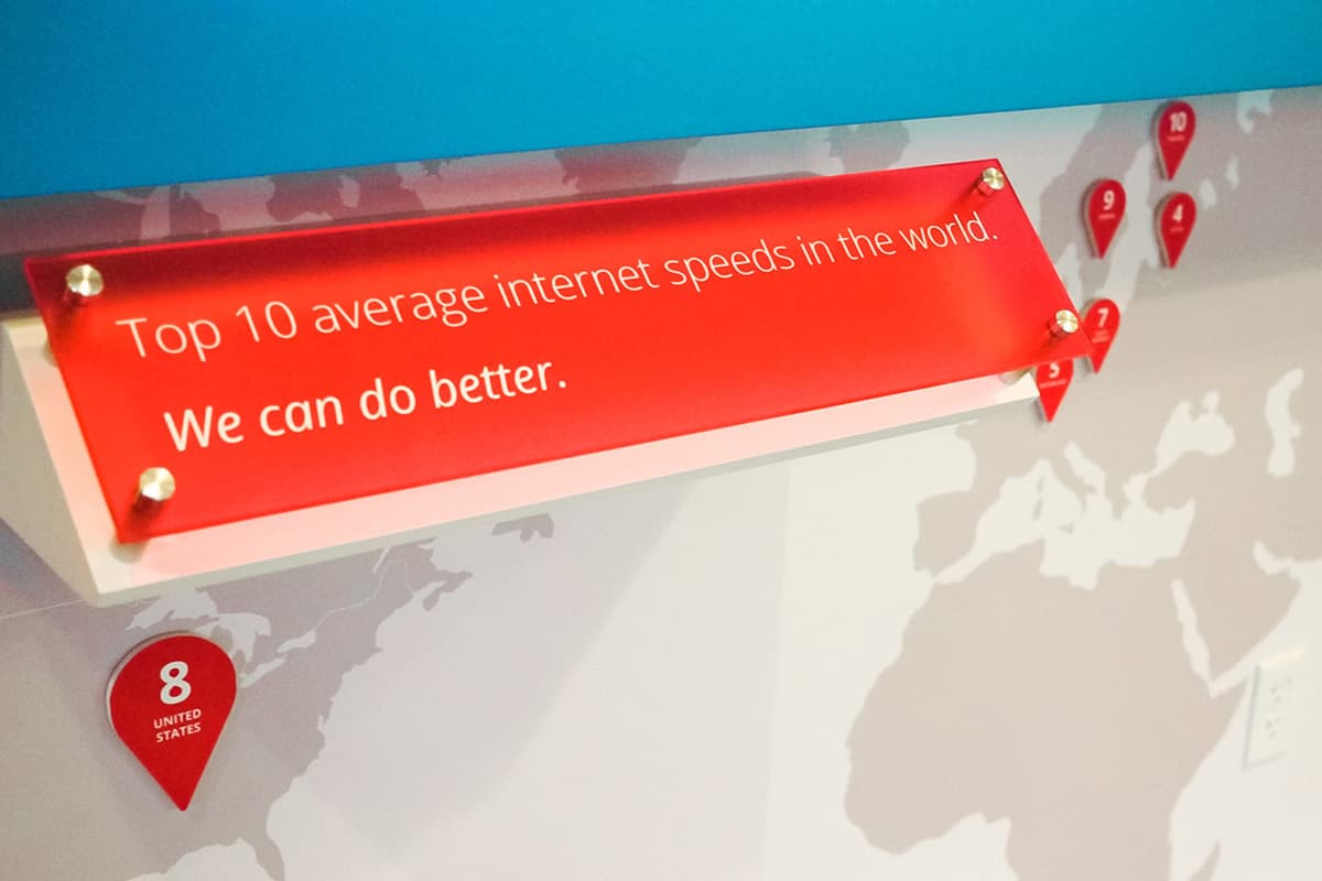 A map shows various geographic locations marked with red pins indicating internet speeds. A red sign reads, "Top 10 average internet speeds in the world. We can do better." The pinned 8 the United States is visible near the bottom-left corner of the image.