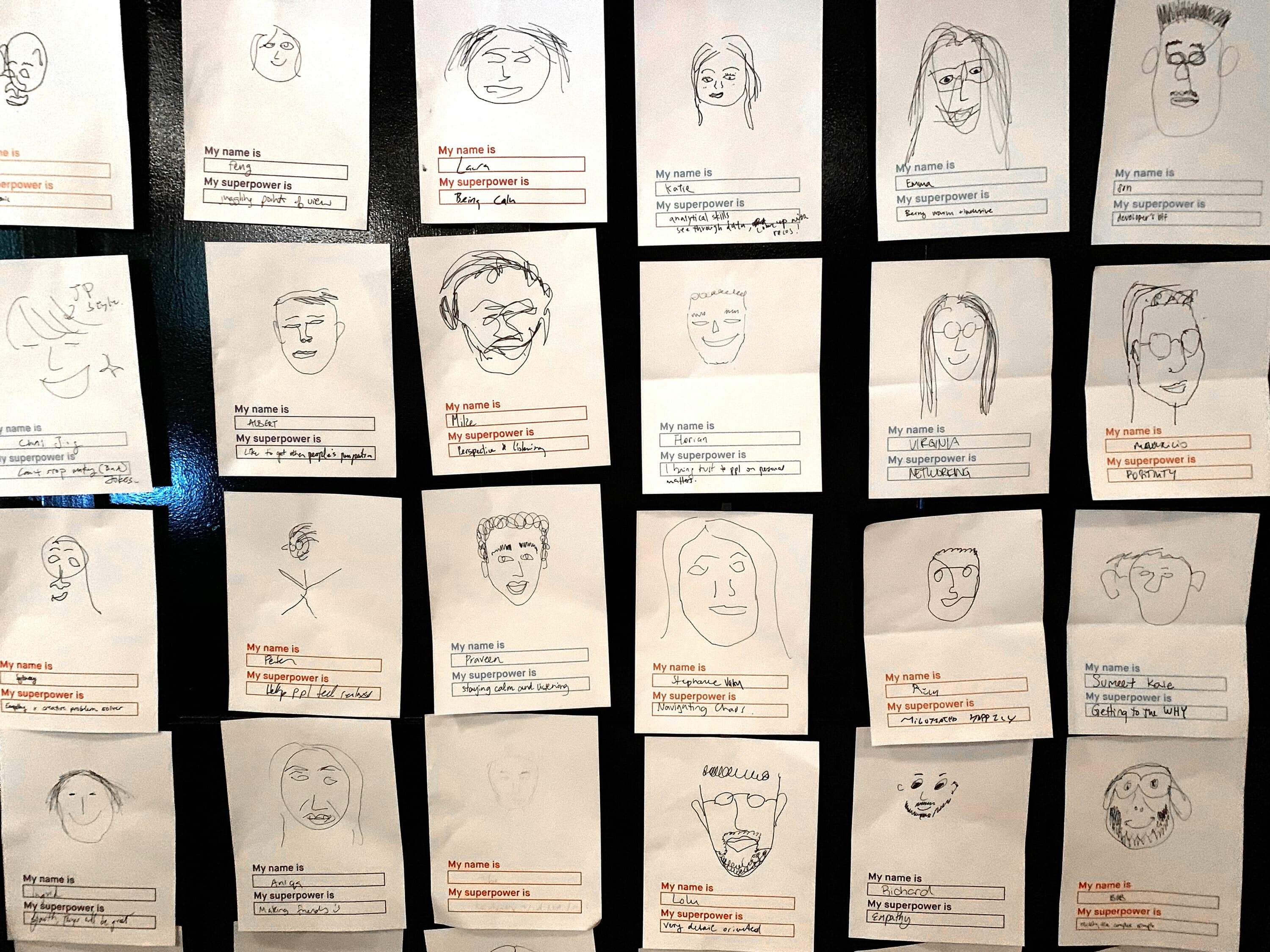 A bulletin board displays 24 sheets of paper, each showcasing a hand-drawn self-portrait. Below each drawing, there are name prompts and fields filled in with various handwritten names, superpowers, and family member labels. The illustrations vary in style and detail.