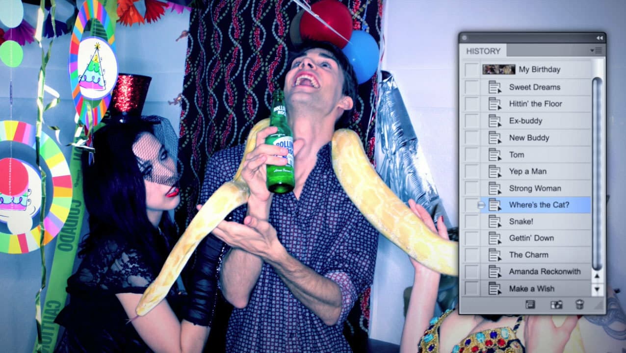 A man at a party, holding a green beer bottle, has a large yellow snake draped around his neck. A woman in a black hat and veil and another person in a colorful top are also present. A screen showing a list of files with playful names is on the right side. Decor includes balloons and streamers.
