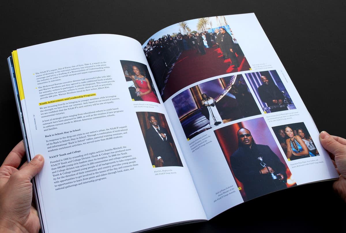 Two hands holding an open book displaying pages with text and multiple photographs. The right page shows images of people at events, some on stage and others in formal attire on a red carpet. The left page contains text in paragraphs, headings, and images.