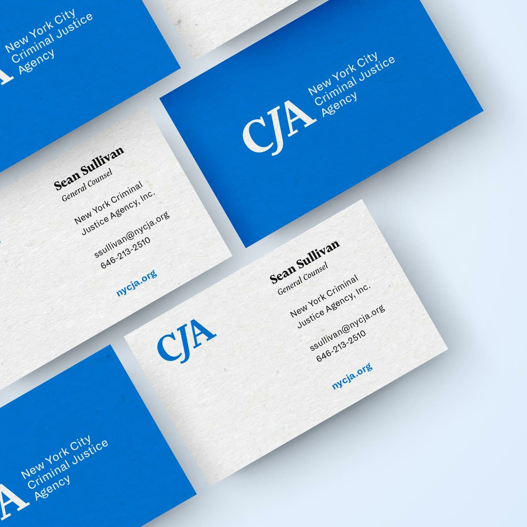 A display of business cards for the New York City Criminal Justice Agency (CJA). The cards are a mix of blue and white with text in white or black. Details include a name, position, contact information, and agency website.
