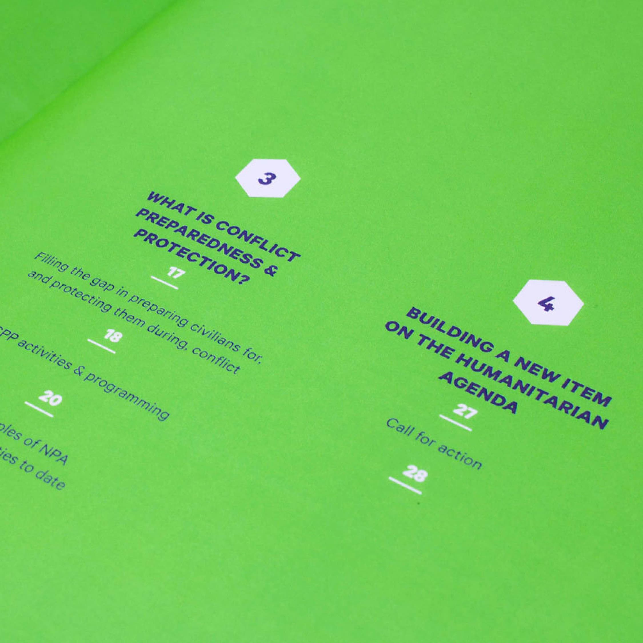 A green booklet spread shows two chapter titles: "What is Conflict Preparedness & Protection?" on the left, and "Building a New Item on the Humanitarian Agenda" on the right. Both titles have corresponding page numbers and subheadings.