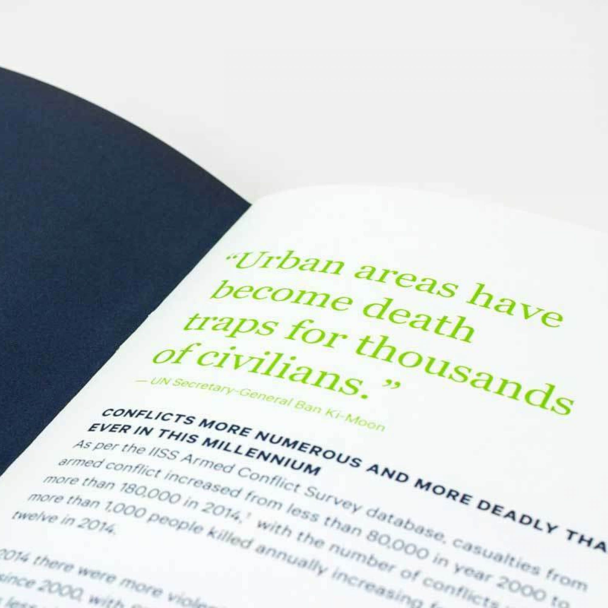 An open book with a quote in green text reading, "Urban areas have become death traps for thousands of civilians." - UN Secretary-General Ban Ki-Moon. Below, there is smaller black text detailing conflicts and their impact on civilians in urban areas.
