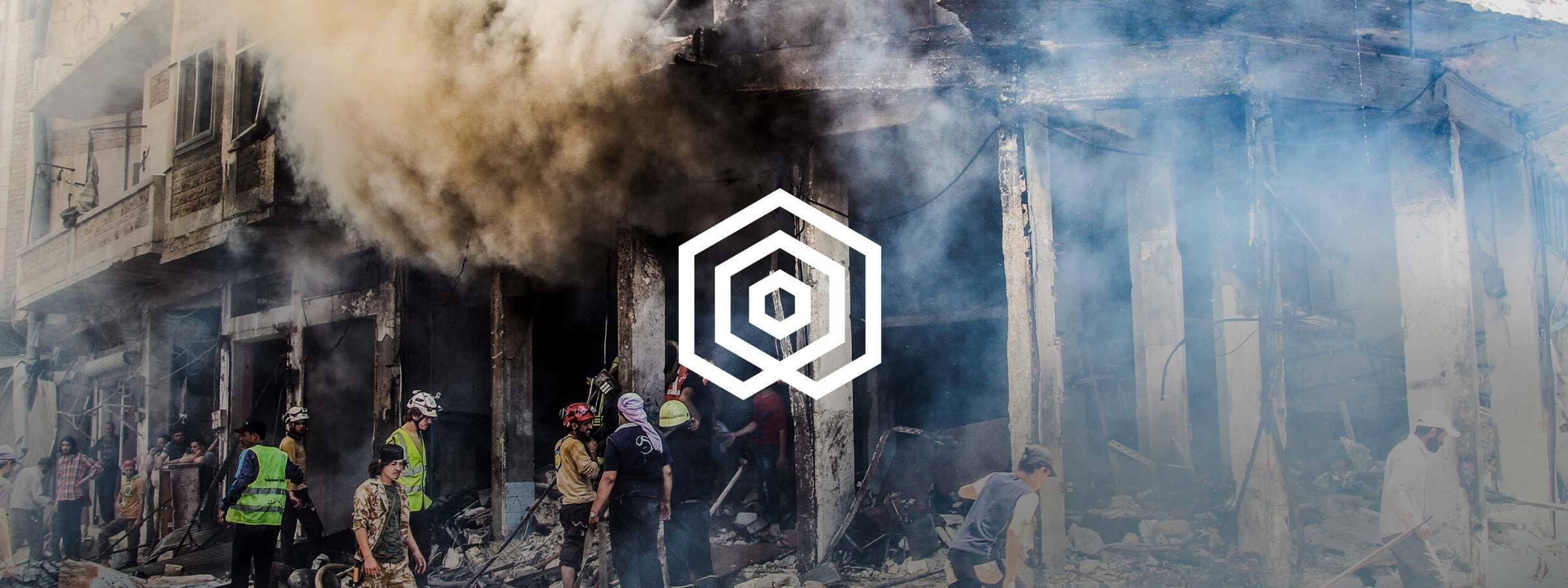 A group of people, including emergency responders, are seen among a partially destroyed building with heavy smoke and debris. The scene depicts a recent disaster or conflict. The image is overlaid with a white geometric logo in the center.