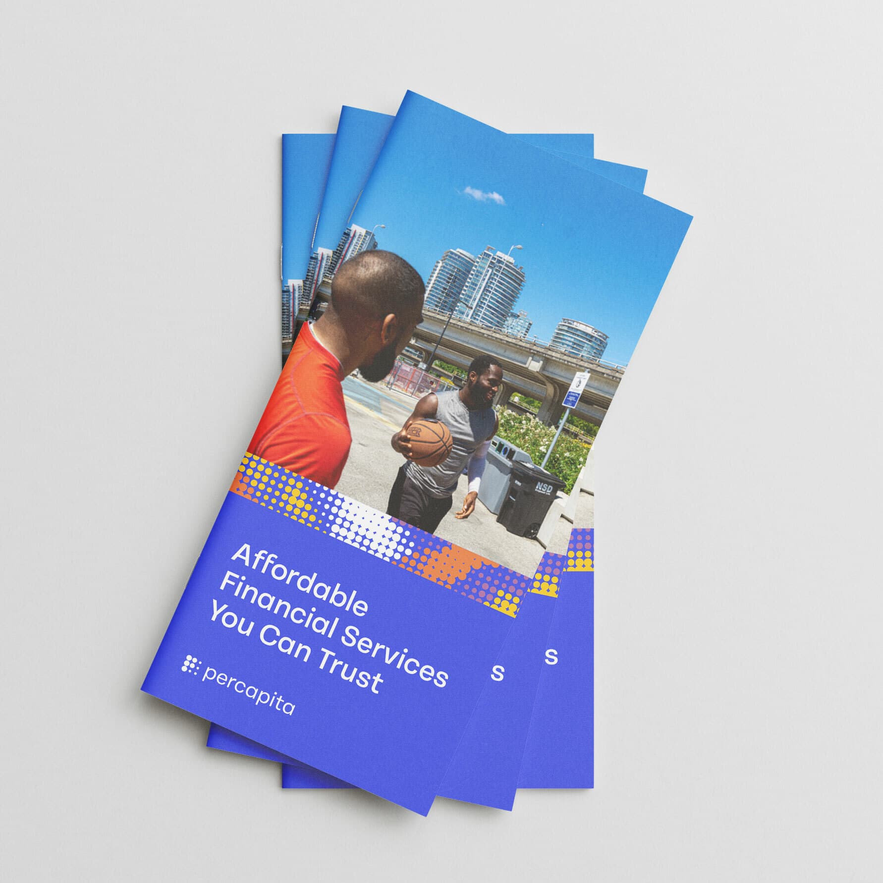 A set of three identical brochures are fanned out on a white surface. The cover image shows a man holding a basketball, standing outdoors with a cityscape in the background. The text on the brochure cover reads, "Affordable Financial Services You Can Trust" followed by a logo and the word "percapita.