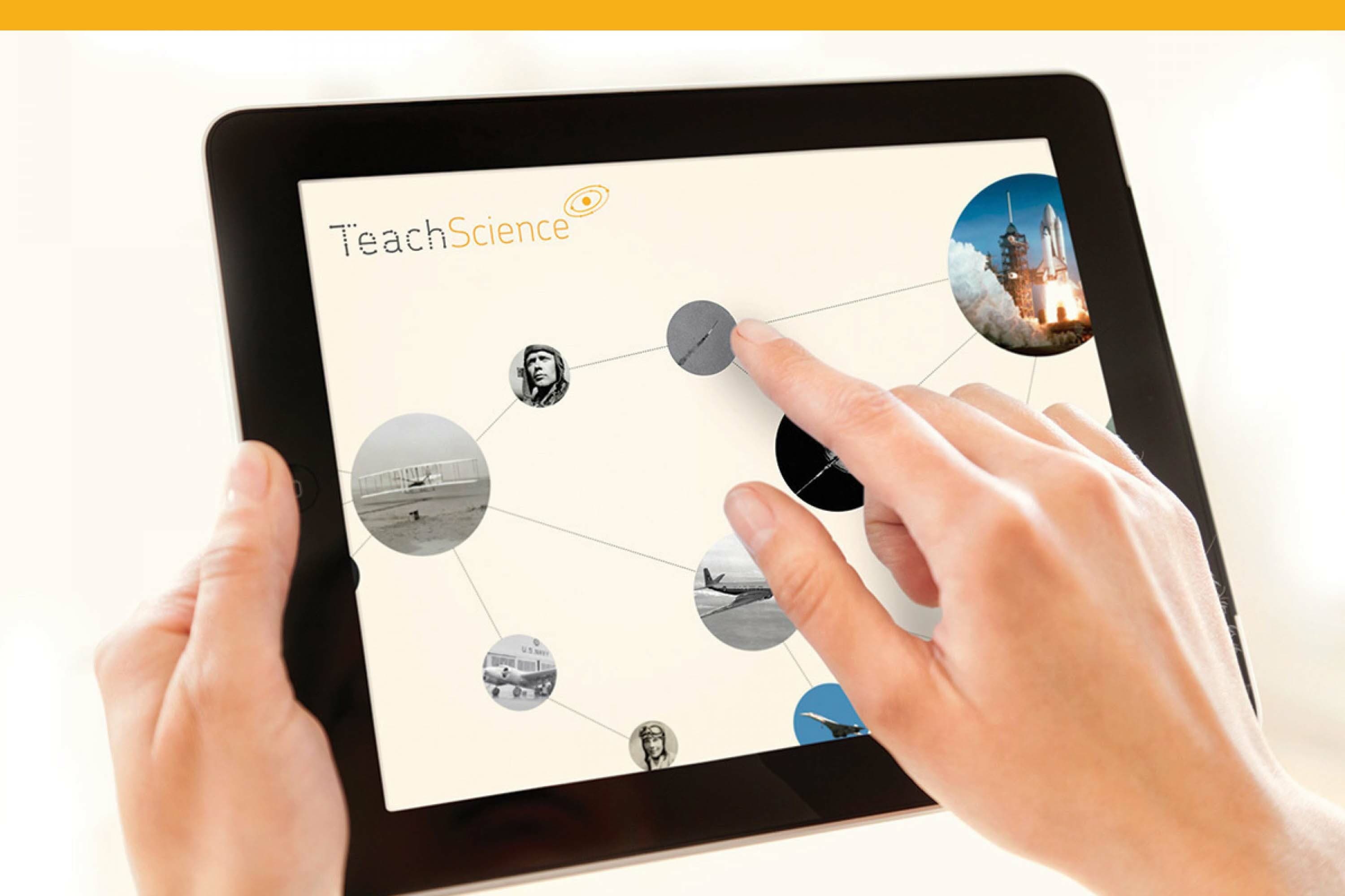 Two hands are holding and interacting with a tablet displaying a TeachScience app. The screen shows a network of interconnected circular images, including a rocket launch and an aviator. One finger is about to touch one of the circles.