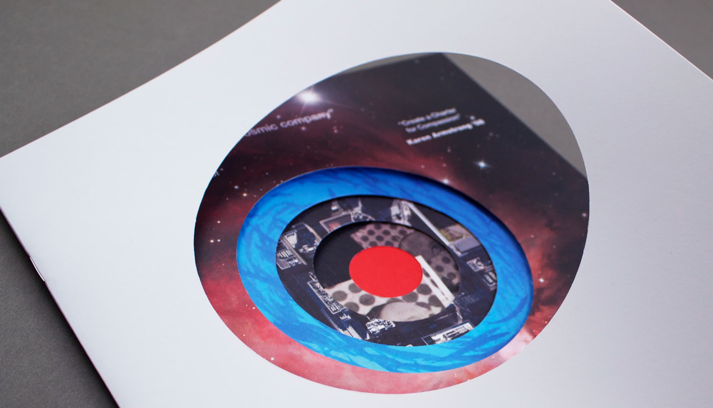 A close-up shot of an open book featuring a colorful circular cutout design. The cutout reveals multiple layers of circles in blue, black, and red, with a celestial background of stars, giving a dynamic, three-dimensional effect.