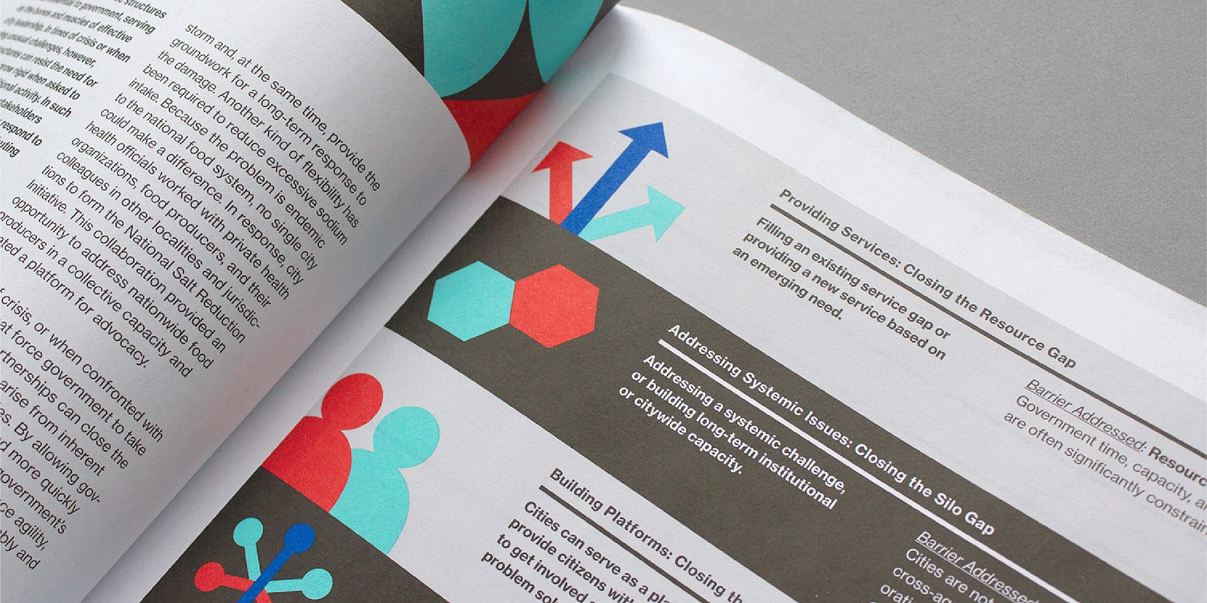 Close-up of a magazine or brochure opened to a page containing text and colorful graphics. The designs include abstract shapes such as circles, arrows, and hexagons in red, blue, and teal. The layout is organized with sections of text and visual elements for emphasis.