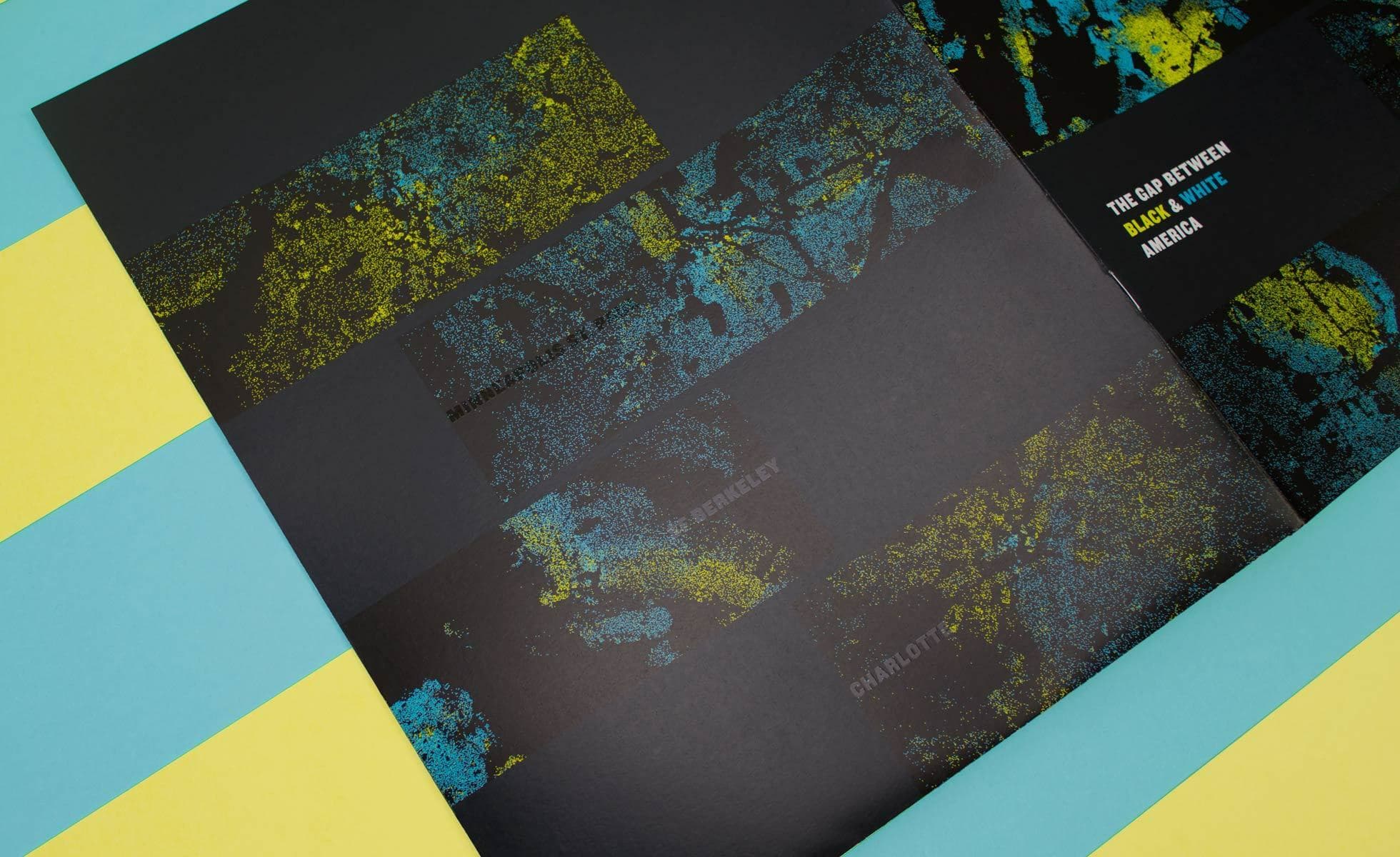 An abstract artistic booklet is open displaying dark pages with splashes of bright yellow and blue paint patterns. Text on the right page reads "THE GAP BETWEEN BLACK & WHITE MUSICALLY." The booklet is placed on a background of alternating yellow and blue stripes.