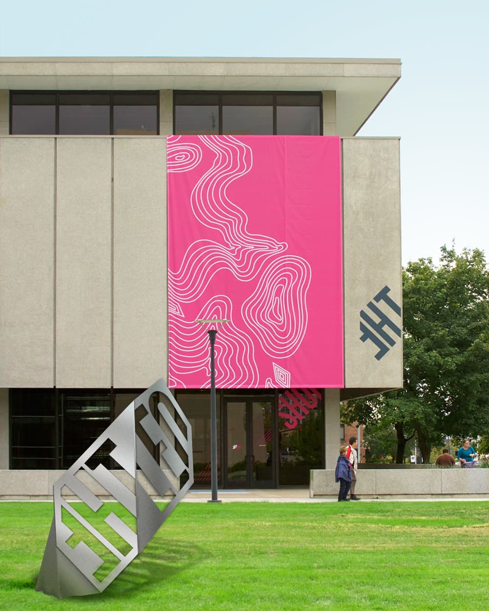 A modern building with large windows and a gray facade features a bold, pink banner adorned with wavy white line patterns. In front of the entrance, a person walks by a metallic sculpture on a grassy lawn. Trees and a clear sky are visible in the background.