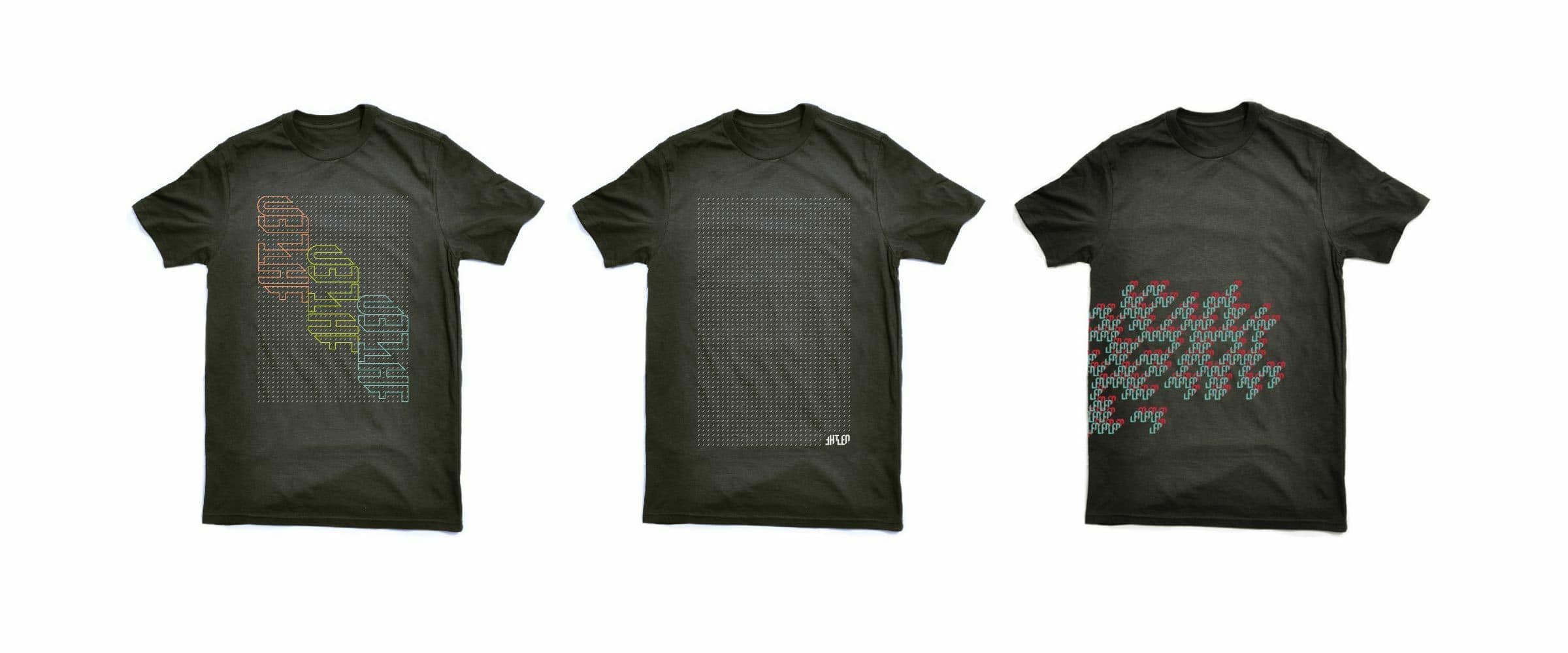 Three black t-shirts displayed in a row. The first t-shirt has a colorful overlapping word design. The second t-shirt has a grid-like pattern. The third t-shirt has a diagonal pixelated pattern in shades of red and blue.