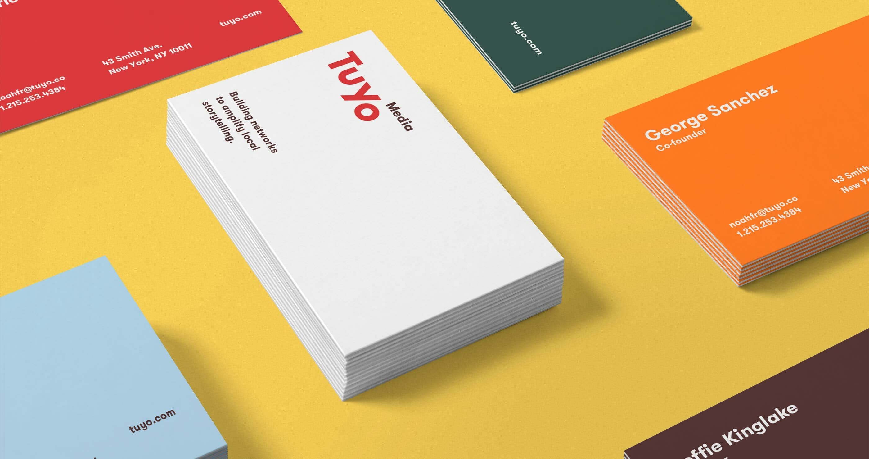 A variety of business cards are spread out on a yellow surface. The central pile features the "Tuyo Media" logo prominently in red. Other cards display names, job titles, and contact details in different colored cards like red, green, blue, and orange.