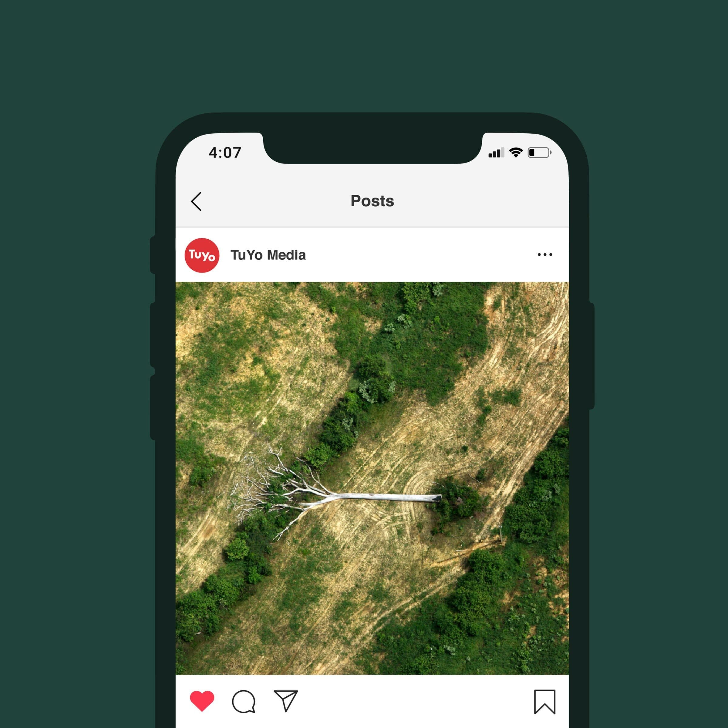 A top view of a smartphone showing an Instagram post by TuYo Media. The image in the post captures an aerial view of a stark white tree lying horizontally in a green and brown landscape. The phone's screen displays a time of 4:07 and a single heart icon underneath the post.