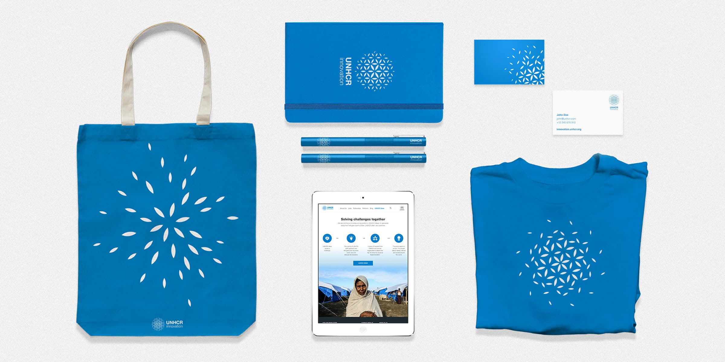 A collection of branded items includes a blue tote bag, two pens, a notebook, a T-shirt, business cards, and a tablet displaying a website. Each item features a white geometric pattern and logo with "UNHCR" text on the bottom. The background is plain white.
