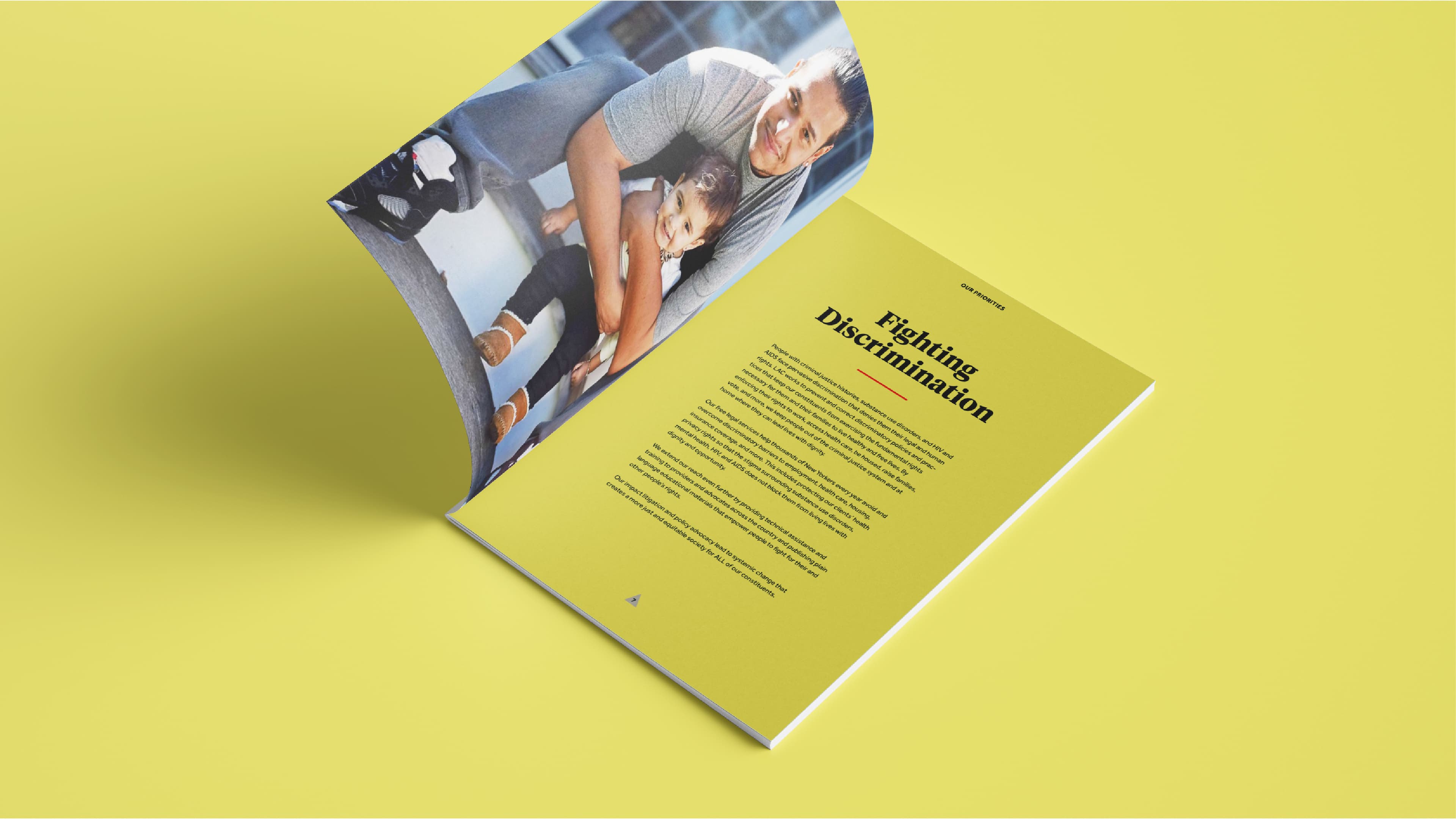 An open magazine on a yellow background. The left page features a photo of an adult holding a child. The right page has the title "Fighting Discrimination" in bold, followed by several paragraphs of text.